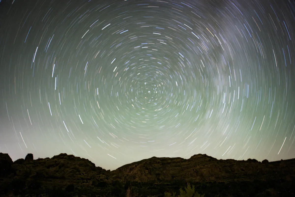 Star trails circling above a dark stone ridge